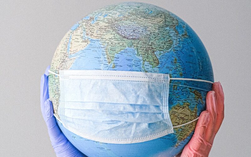 Hands With Latex Gloves Holding a Globe with a Face Mask